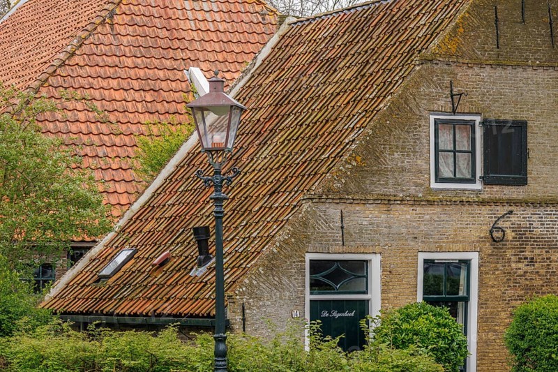 Quiet village street with characteristic brick houses and nostalgic street lamp, old houses with green gardens in a small village, nes, ameland, the netherlands