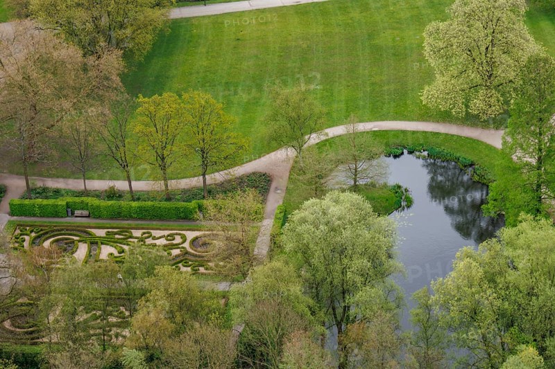 A green park with footpaths, a pond and trimmed hedges, surrounded by trees in spring, small park with green trees and paths between tall houses, Rotterdam, Netherlands