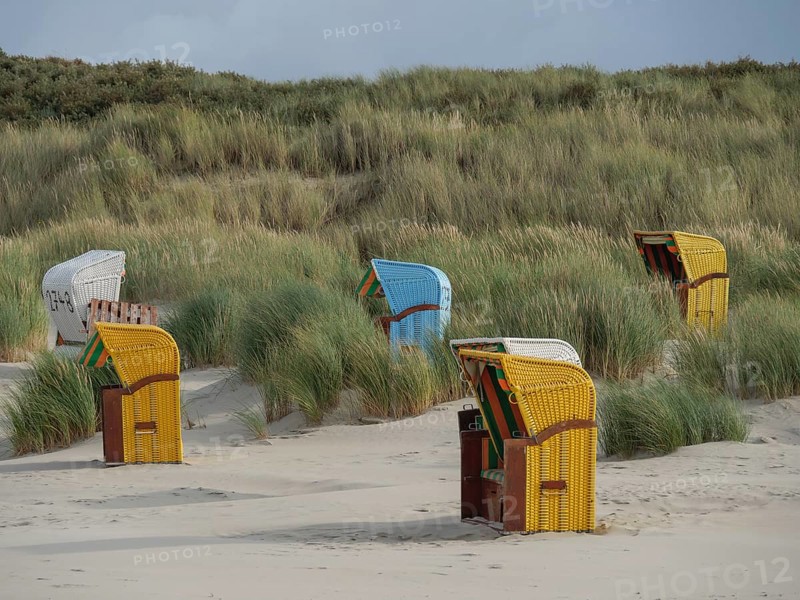 Colourful beach chairs stand at intervals along the dunes, surrounded by grass and under partly cloudy skies, colourful beach chairs on the beach and in the dunes under cloudy skies, red wooden boat and yellow beach chair, Juist, Germany, Europe