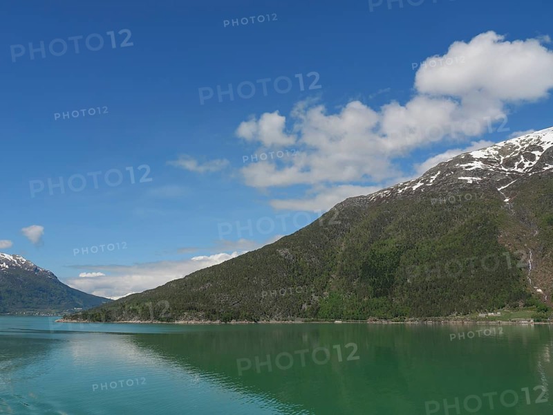 Clear water, snow-capped mountains and blue sky in a peaceful landscape, greenish shimmering water in a fjord with snow-capped mountains and green trees, eidfjord, Norway, Europe