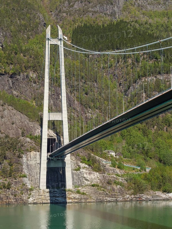 Close-up of a large bridge crossing a wide river and through rocky mountain landscapes, bridge in a fjord with snow-capped mountains and green trees, greenish shimmering water, eidfjord, Norway, Europe