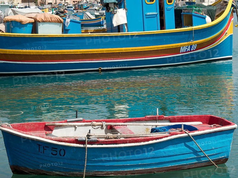 A small red boat and a larger fishing boat moored in the harbour, many colourful fishing boats in a harbour in the Mediterranean, Marsaxlokk, malta