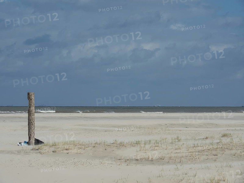 Lonely beach with dunes in front of a grey, cloudy sky. The sea is calm and spacious, waves on a beach, sunny day with clouds in the sky over the sea, Spiekeroog, GERMANY