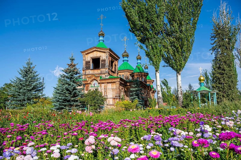 Colourful flowers in front of the Russian Orthodox Church Cathedral of the Holy Trinity, wooden church with green spires, Karakol, Kyrgyzstan, Asia