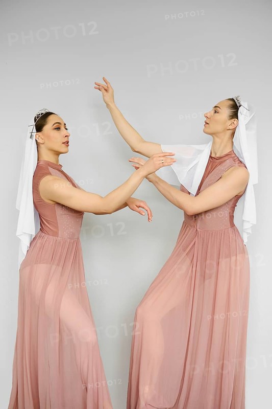 Two beautiful ballerinas practicing in front of each other over grey wall