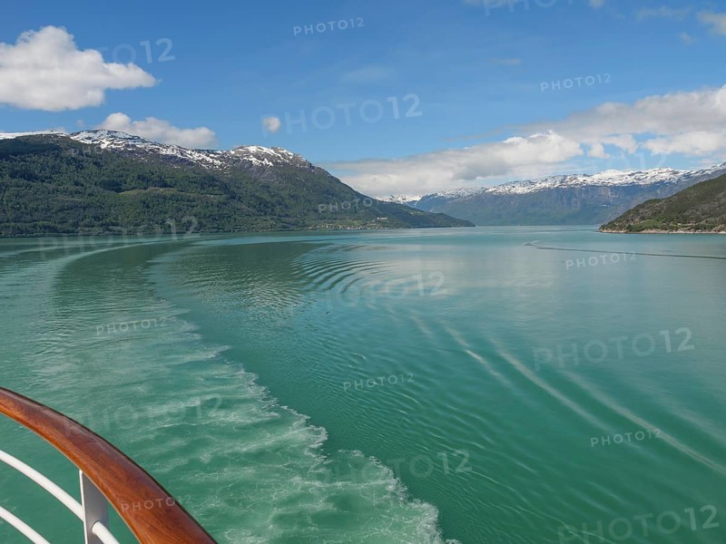 Boat trip on a clear water surrounded by snow-capped mountains and blue sky, greenish shimmering water in a fjord with snow-capped mountains and green trees, eidfjord, Norway, Europe