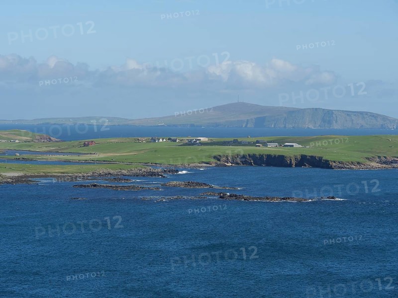 View of the azure blue sea, where green fields reach to the rocky coast, green meadows on a deep blue sea and a rocky coastline with individual houses, lerwick, shetland, Scotland, United Kingdom, Europe