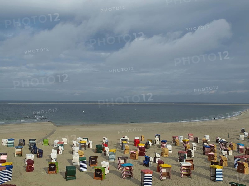 A long sandy beach with many colourful beach chairs and calm sea in the background, beach chairs and beach tents by the sea under a cloudy sky, boardwalk in the sand, Borkum, germany