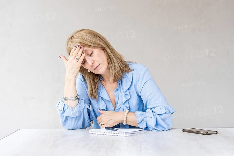 A mid-adult blonde woman is holding one hand on her forehead