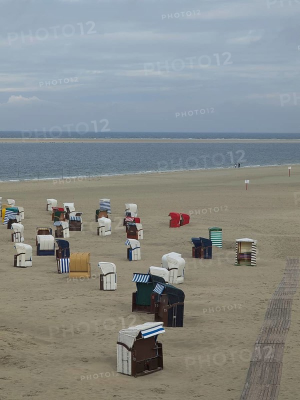 Single beach chairs are scattered on the empty, quiet beach under a cloudy sky, beach chairs and beach tents by the sea under a cloudy sky, boardwalk in the sand, Borkum, germany