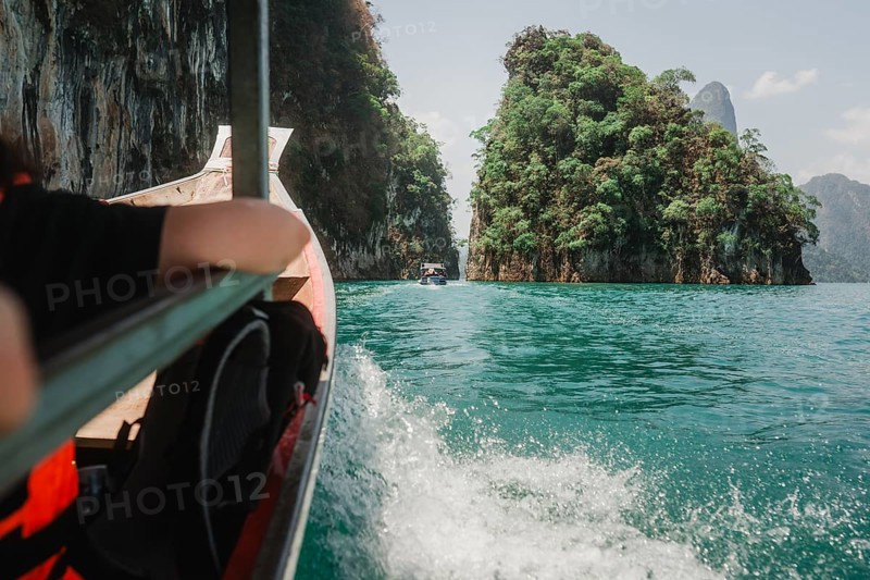 Boat surrounded by emerald green water and wooded cliffs. Khao Sok National Park, Thailand, Asia