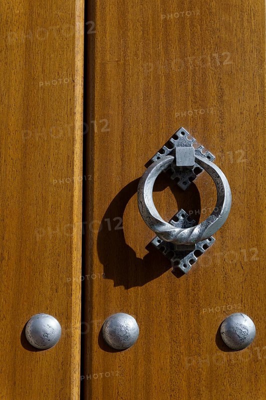 Latch on a wooden door with metal rivets illuminated by sunlight with shadows