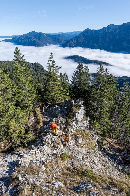Two friends, mountaineers climbing the via ferrata to the rocky summit of the Ettaler Manndl, view over mountain landscape and sea of clouds, high fog in the valley, Ammergau Alps, Bavaria, Germany, Europe