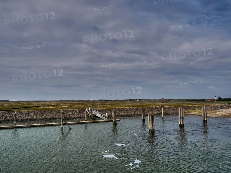 A long jetty in the sea with a cloudy sky and coastal landscape in the background, small jetty with a mono-sea sailing boat in the north sea against a cloudy sky, spiekeroog, germany