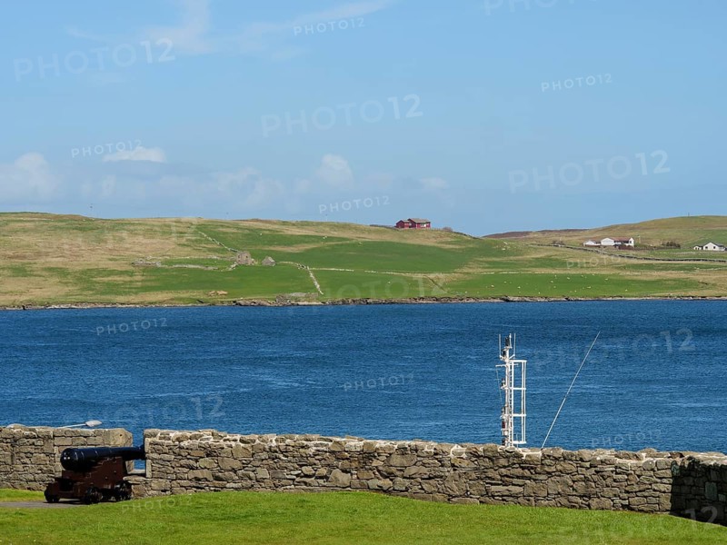 Old cannon in front of a stone wall with a view of the sea and green hills under a blue sky, old cannon on a stone wall by the sea against a blue sky, lerwick, Scotland, United Kingdom, Europe