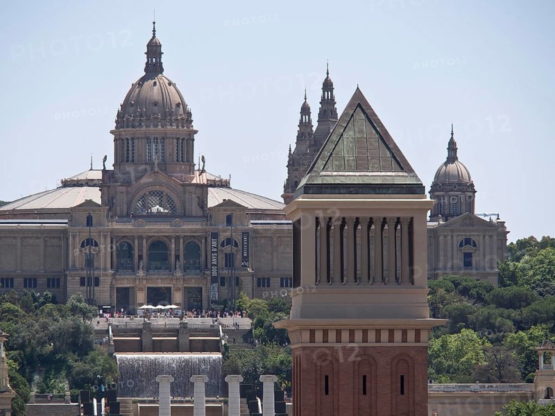 Close-up of a historic building with a magnificent dome and detailed tower against the background of a clear sky, two red towers against the panorama of a large city, Barcelona, Spain, Europe