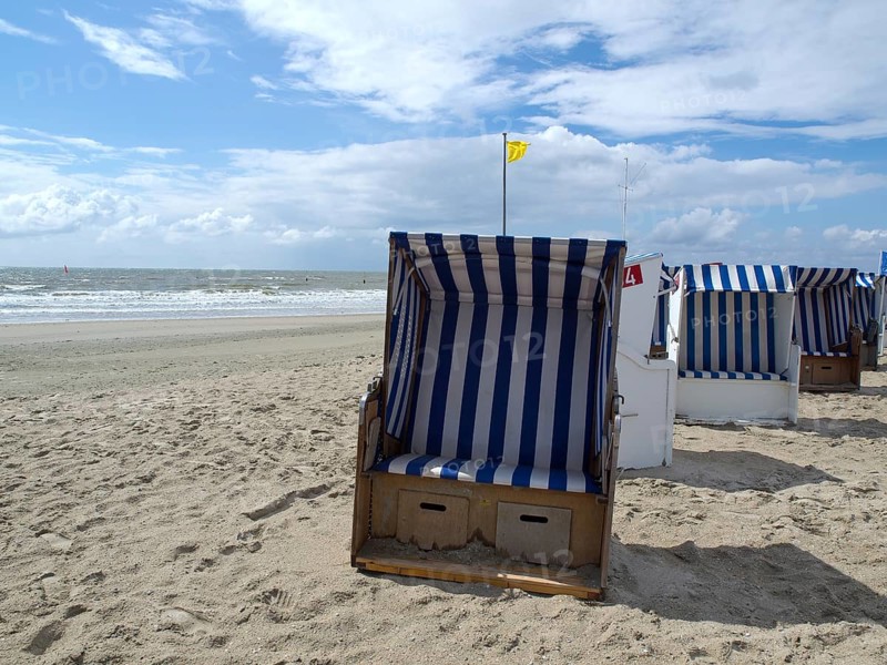 A single blue and white beach chair stands on the beach under a partly cloudy sky, blue and white striped beach chairs on the beach, Norderney, Germany, Europe