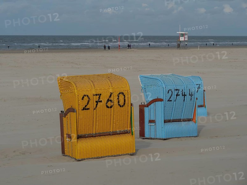 A yellow and a blue beach chair stand close to each other with a view of the sea, colourful beach chairs on the beach and in the dunes under a cloudy sky, red wooden boat and yellow beach chair, Juist, Germany, Europe
