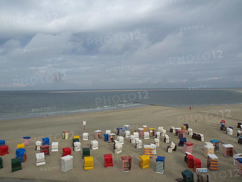 Colourful beach chairs stand abandoned on the beach while the sea and the clouds form the horizon, beach chairs and beach tents by the sea under a cloudy sky, boardwalk in the sand, Borkum, germany