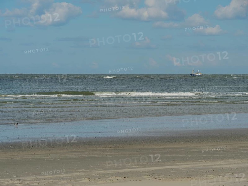 Seascape with a boat in the distance, gentle waves and wide sandy beach, beach and dunes with grass and a bench by the sea, nes, ameland, the netherlands