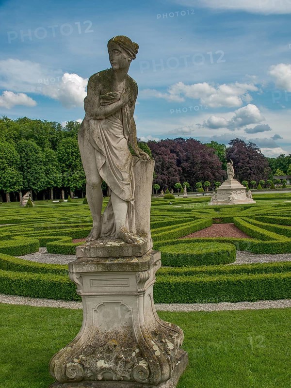 Stone statue of a woman in a well-kept baroque garden with symmetrical hedges and cloudy sky, park with green hedges, small paths and old statues, nordkirchen, germany