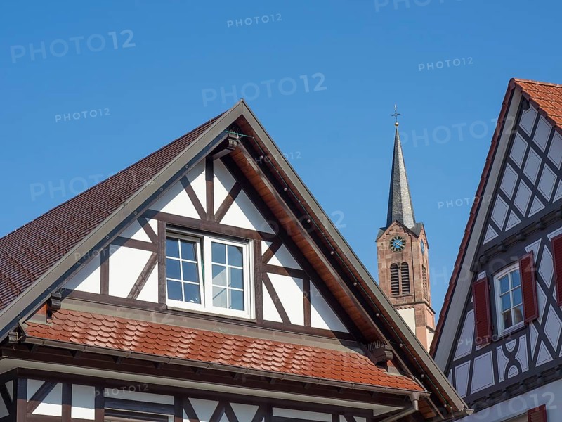 Detail of a half-timbered house with a view of a church tower under a bright blue sky, old half-timbered houses with flower decorations in summertime, Freudenstadt, Germany, Europe