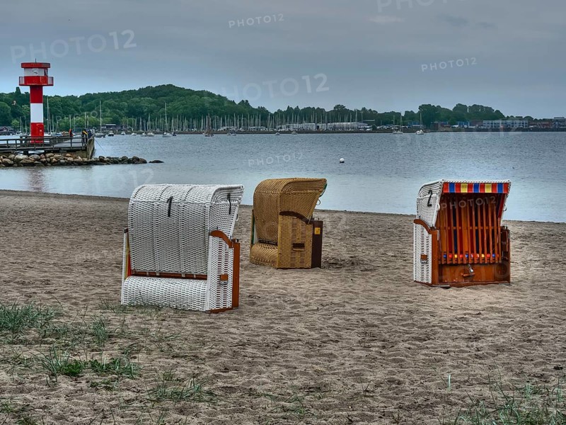 Several beach chairs standing on a cloudy beach, behind them a lighthouse and calm sea under a cloudy sky, beach chairs on a quiet sandy beach by the sea, clouds over the sea, Eckernfoerde, germany