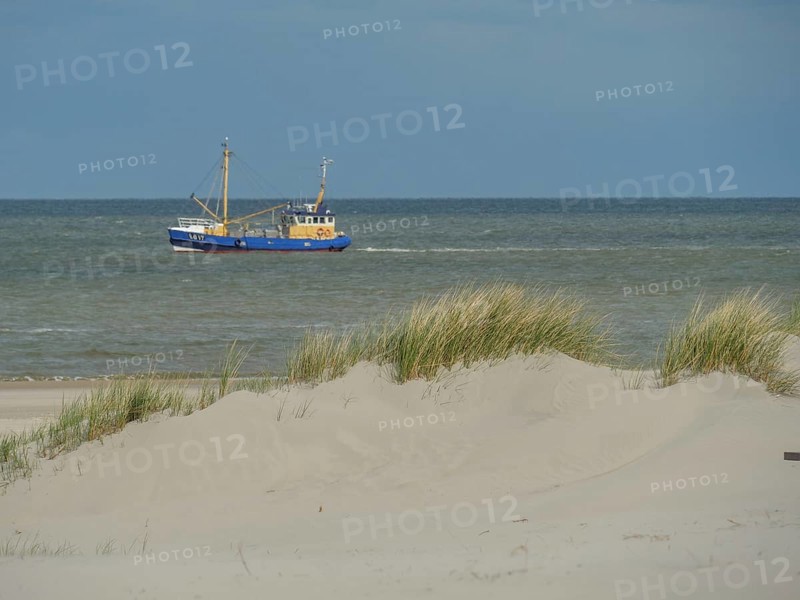 A fishing boat on the sea, surrounded by dunes and sand under a cloudy sky, dunes on an island with a blue boat and a bench, clouds and sand by the sea, nees, ameland, the netherlands