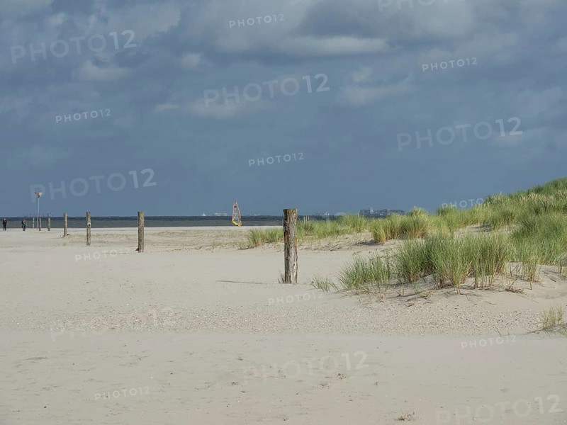 Sand dunes with tufts of grass and posts on the beach, distant windsurfers in the background, lonely beach with dune grass in the neighbouring dunes and marker posts, clouds playing in the sky, Spiekeroog, Germany, Europe