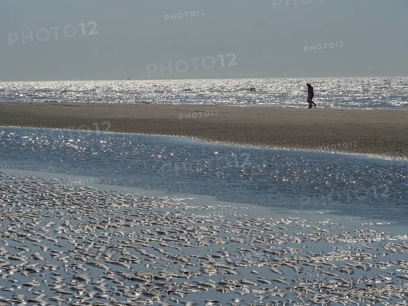 Single person walking along a wide beach with reflecting watercourse, glittering sea water at low tide on the beach, de haan, belgium