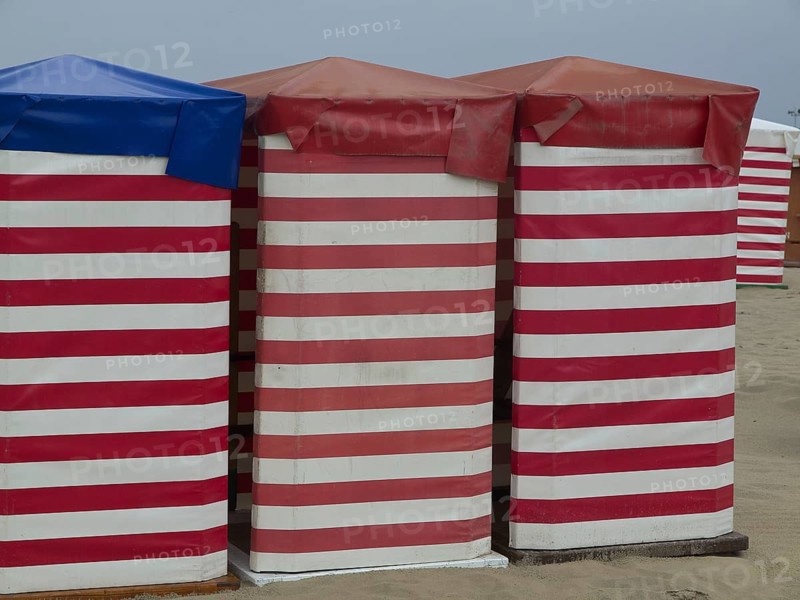 Three colourful beach huts with striped pattern stand on the sandy beach, beach chairs and beach tents by the sea under a cloudy sky, boardwalk in the sand, Borkum, germany