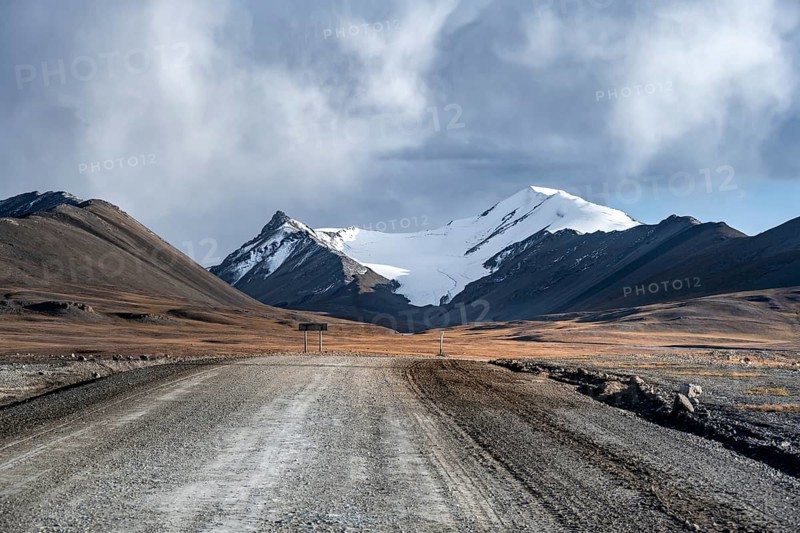 Gravel road through autumnal plateau, glaciated and snow-covered peaks, Sary Tor Glacier, Ak Shyrak Mountains, near Kumtor Gold Mine, Tian Shan, Kyrgyzstan, Asia