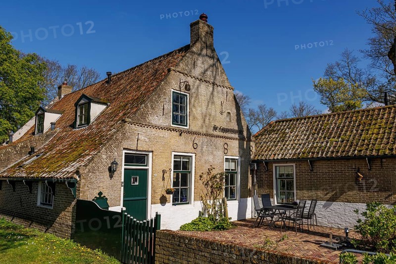An old house with tiled roof and terrace, surrounded by green plants on a sunny day, historic houses in a small village with small streets and trees in spring, Nes, Ameland, Netherlands