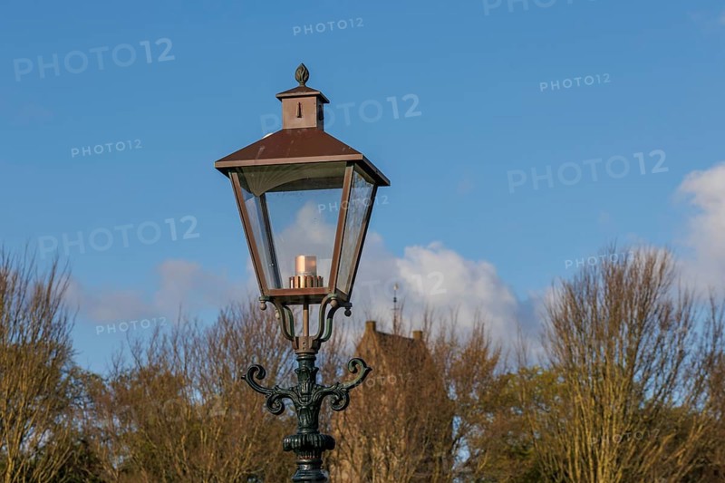 Classic street lamp against a clear blue sky and bare trees in the background, old houses and small streets with lanterns and green trees, Nes, Ameland, Netherlands