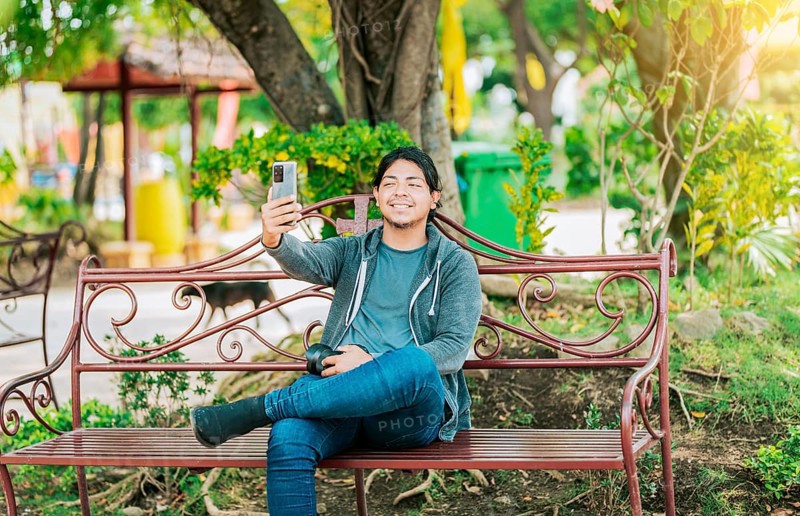 Relaxed guy taking a selfie sitting on a bench at sunset. Smiling man sitting on a bench taking a selfie in Nagarote Park