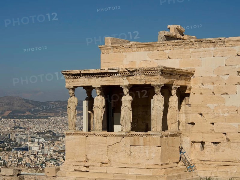 The Erechtheion with the Caryatid statues and a cityscape in the background under a clear sky, historical columns and ruins at an ancient site against a blue sky, Athens, Greece, Europe