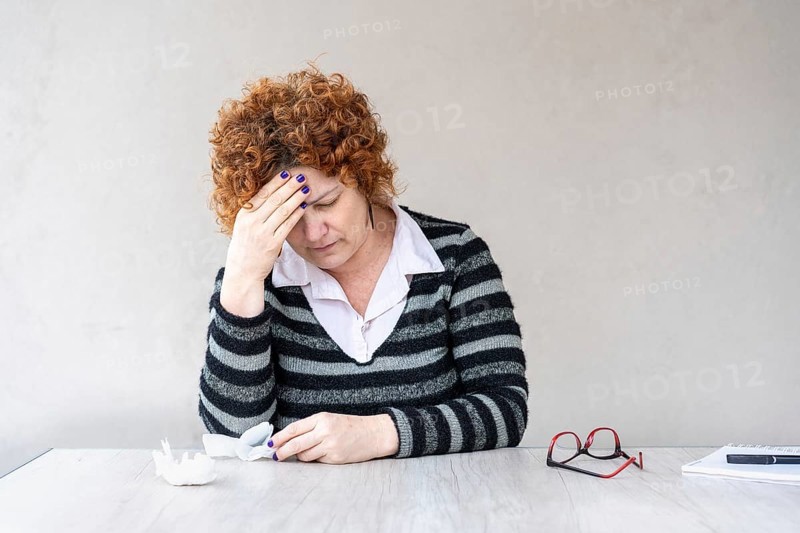 A mid-adult redhead woman is holding one hand on her forehead