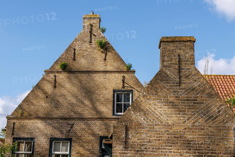 Traditional brick house with windows and chimney in front of a blue sky and scattered clouds, historic house gables with windows in a cloudless sky