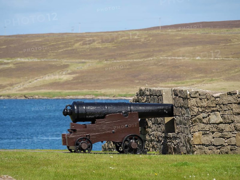 Historic cannon in front of a stone wall with sea view and a hill in the background, old cannons on a stone wall by the sea against a blue sky, lerwick, Scotland, United Kingdom, Europe