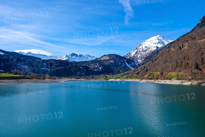 Lake Lungern surrounded by snow-capped mountains and green hills under a blue sky, Lungern, Obwalden, Switzerland, Europe