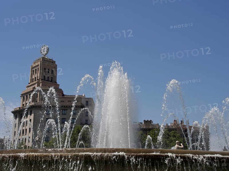 A fountain with powerful water jets in front of a historic building under a blue sky, fountain with figures in front of a historic building, barcelona, spain