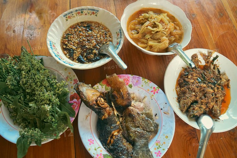 Overhead view of an authentic traditional thai meal of grilled catfish or pla duk yang, sour bamboo soup or Keng No Mai, tamarind dipping sauce and neem tips on a wooden table. Uttaradit, Thailand, Asia