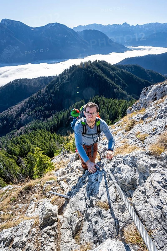 Hiker on via ferrata to Ettaler Manndl, view over mountain landscape and sea of clouds, high fog in the valley, Ammergau Alps, Bavaria, Germany, Europe
