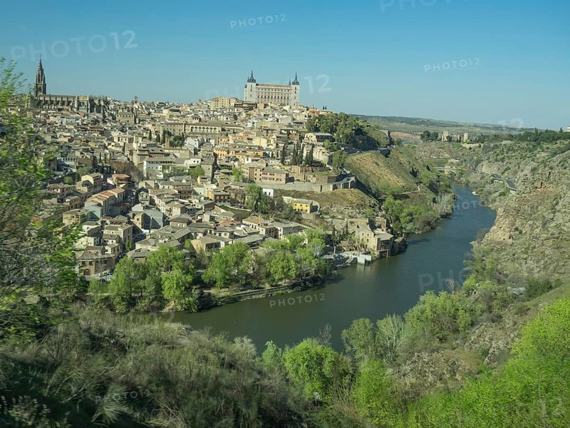 Historic city on the river with impressive architecture and striking church towers, situated on a hill under a blue sky, historic city with old houses and large churches on a small river in front of a blue sky, toledo, spain