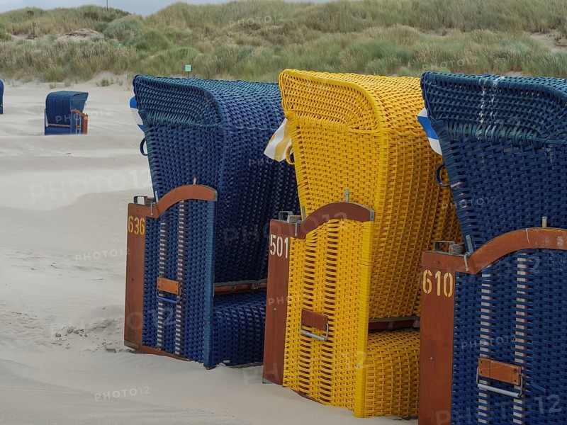 A row of colourful beach chairs on the sandy beach under a cloudy grey sky, colourful beach chairs on the beach and in the dunes under an overcast sky by the sea, Juist, Germany, Europe