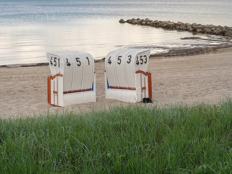 Two white beach chairs in front of a green meadow, sandy beach and calm sea in the background, beach chairs on a quiet sandy beach by the sea, clouds over the sea, Eckernfoerde, germany
