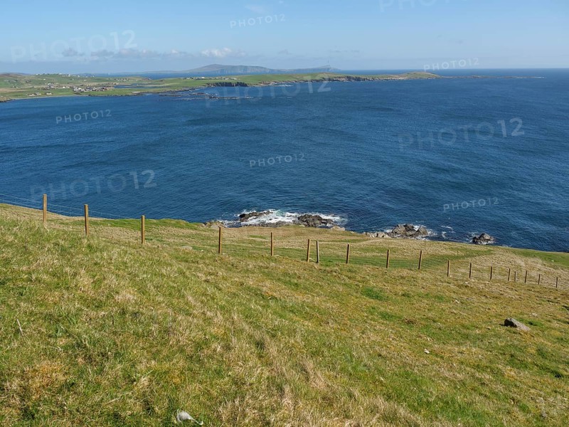 Green hills with a fence reaching to the blue sea, green meadows by a deep blue sea and a rocky coastline with individual houses, lerwick, shetland, Scotland, United Kingdom, Europe
