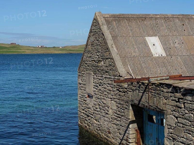 Stone clad building on the water's edge with sea and sky in the background, old stone house on the blue sea against a blue sky, Lerwick, Scotland, United Kingdom, Europe