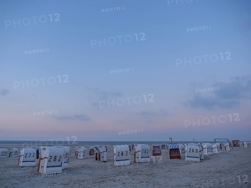 A peaceful scene on the beach with white and striped beach chairs during dusk, setting sun on a beach with beach chairs and clouds in the sky, spiekeroog, germany