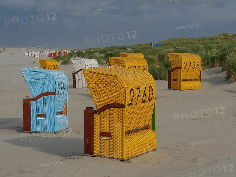 View of colourful beach chairs in front of cloudy sky, some baskets in the sand with dune grass, colourful beach chairs on the beach and in the dunes with cloudy sky, red wooden boat and yellow beach chair, Juist, Germany, Europe